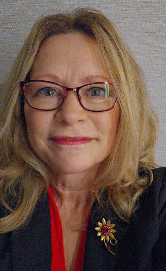 Woman with glasses and a floral brooch.